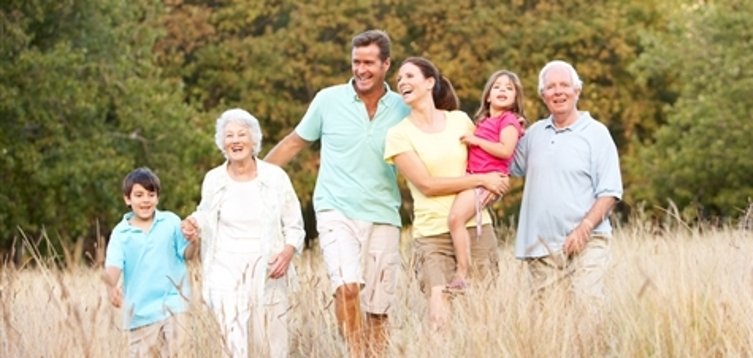 Sechs Personen unterschiedlichen Alters gehen gemeinsam durch ein hohes Grasfeld vor einem bewaldeten Hintergrund.