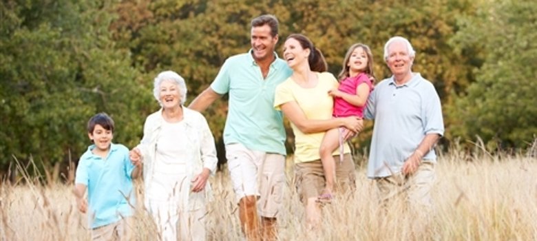 Sechs Personen unterschiedlichen Alters gehen gemeinsam durch ein hohes Grasfeld vor einem bewaldeten Hintergrund.