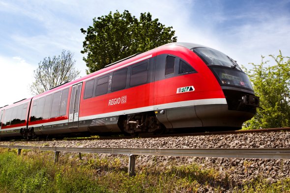 Roter Regionalzug der Deutschen Bahn auf Gleisen vor Bäumen unter blauem Himmel