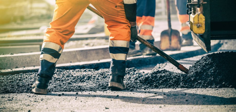 Asphaltarbeiten Beine von Bauarbeitern in Warnkleidung beim Verteilen von frischem Asphalt auf einer Straße