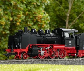 Modell einer Dampflokomotive mit schwarzem Kessel und rotem Fahrwerk auf Gleisen vor grünem Hintergrund