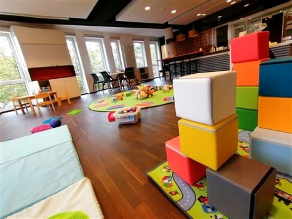 Kinderspielzimmer mit bunten Bauklötzen, Spielteppich und Sitzgelegenheiten vor großen Fenstern