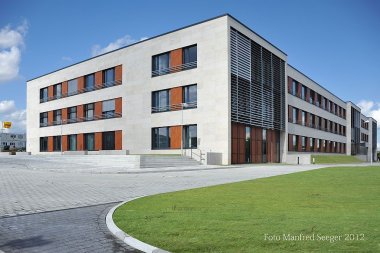 Modernes, mehrstöckiges Schulgebäude mit großen Fenstern und Holzverkleidungen vor blauem Himmel