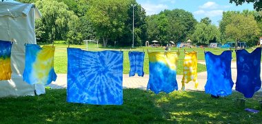 Freizeitangebote Mehrere blaue und gelbe Batik-Tücher hängen an einer Wäscheleine im Freien vor einer Wiese mit Bäumen und Spielplatzgeräten