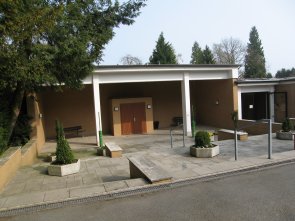 Trauerhalle auf einem Friedhof mit Sitzbänken und Pflanzkübeln