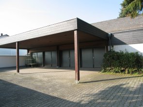 Eingangsbereich einer Trauerhalle mit überdachtem Vorbau und drei geschlossenen Türen
