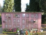 Urnenwand auf einem Friedhof mit mehreren Gedenktafeln, Blumen und Pflanzen davor, umgeben von Bäumen