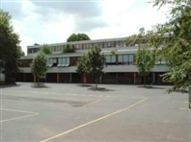 John-F.-Kenney-Schule Schulgebäude mit mehreren Fenstern und einem großen gepflasterten Schulhof im Vordergrund