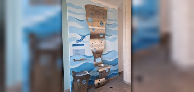 Trinkbrunnen Dorint Skulptur aus Metall mit runden Aussparungen vor einer Wand mit blauen Wellenmustern und Schriftzug 'hassia HEILQUELLE'