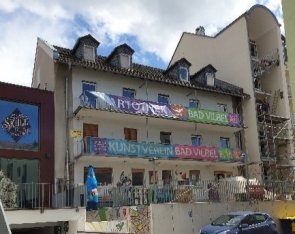 Mehrstöckiges Gebäude mit mehreren bunten Bannern, darunter zwei mit der Aufschrift 'KUNSTVEREIN BAD VILBEL'