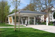 Modernes, verglastes Gebäude mit Flachdach in einem Park mit Bäumen und Rasen