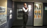 Mann in historischer Kleidung steht in Museumsausstellung mit Texttafeln und Vitrinen mit Keramikflaschen
