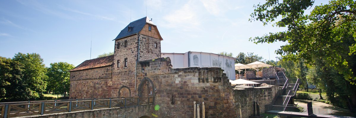 Wasserburg mit steinernem Brückenbogen, Turm mit spitzem Dach bei sonnigem Himmel