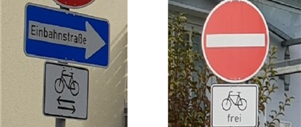 Zwei Verkehrsschilder: links ein blaues Einbahnstraßenschild mit einem weißen Fahrradzusatzschild darunter, rechts ein rotes Durchfahrtsverbotsschild mit einem weißen Zusatzschild 'frei' und Fahrradsymbol.