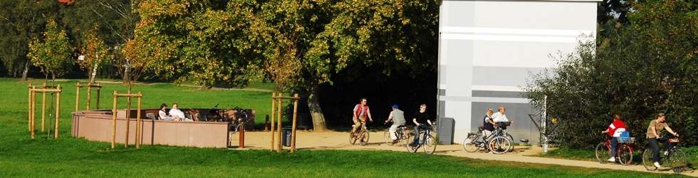 Gruppe von Radfahrern auf einem Weg neben einer Wiese und einem weißen Gebäude im Hintergrund