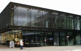 Modernes Gebäude mit Glasfassade und horizontalen Lamellen, davor Menschen und Sitzgelegenheiten