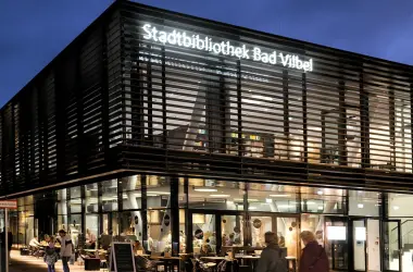 Stadtbibliothek Bad Vilbel Modernes Gebäude der Stadtbibliothek Bad Vilbel mit beleuchtetem Schriftzug und Menschen vor dem Eingang am Abend