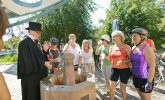 Stadtführer in schwarzem Anzug und Zylinder erklärt einer Gruppe von Radfahrern an einem Trinkbrunnen im Freien
