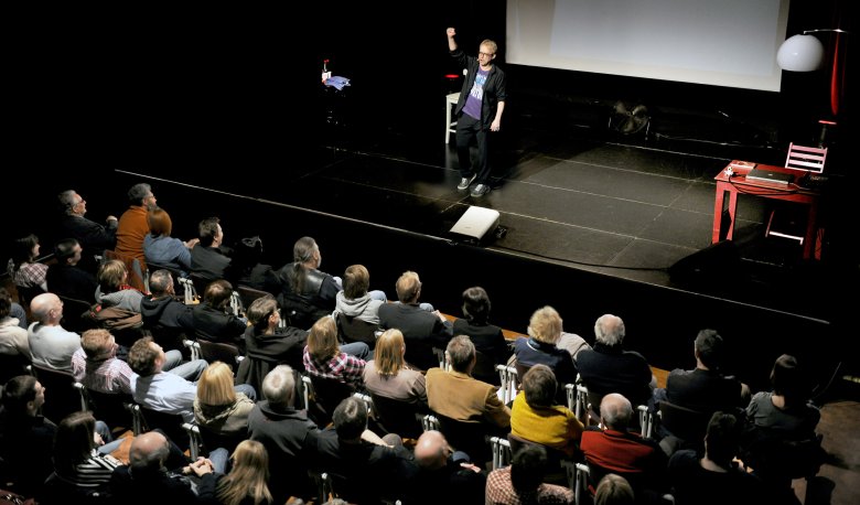 Bühne mit einem stehenden Schauspieler vor einem Publikum in einem Theater.