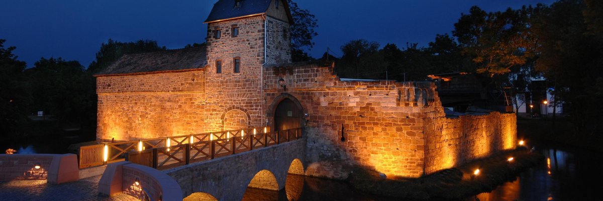 Beleuchtete mittelalterliche Wasserburg bei Nacht unter klarem Himmel mit sichtbarem Vollmond