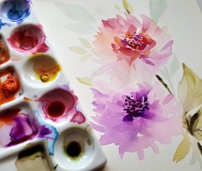 Aquarellpalette mit verschiedenen Farben neben einem Blatt mit floralen Aquarellmalereien