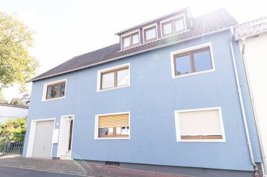 Zweistöckiges Wohnhaus mit blau gestrichener Fassade, mehreren Fenstern und Garage an einer Straße