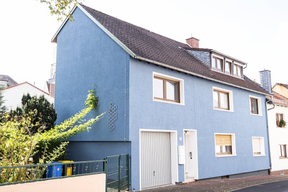 Zweistöckiges Wohnhaus mit blauer Fassade, mehreren Fenstern und einer Garage an der Straßenseite