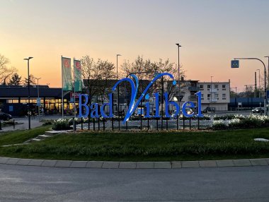 Großes blaues Schriftzug-Logo "Bad Vilbel" auf einem begrünten Kreisverkehr bei Dämmerung