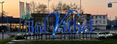 Biwerkreisel Großes blaues Schriftzug-Logo "Bad Vilbel" auf einem begrünten Kreisverkehr bei Dämmerung