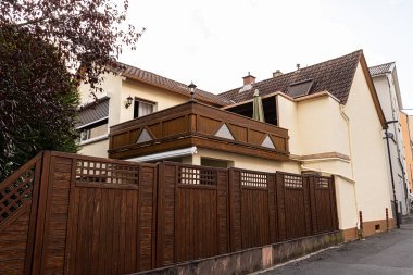 Zweistöckiges Wohnhaus mit braunem Holzzaun und Balkon mit Sonnenschirm an einer Seitenstraße