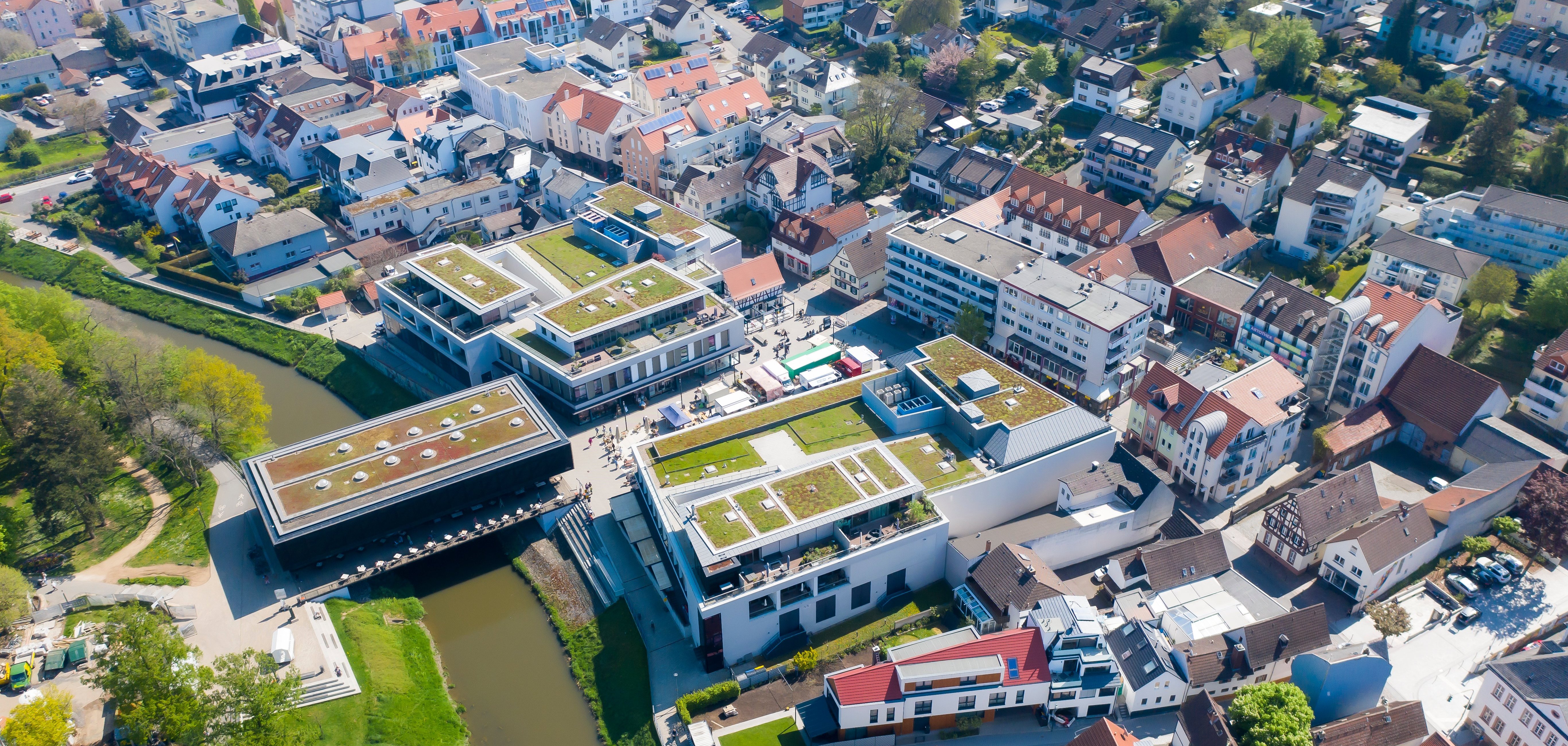 Luftaufnahme von Bad Vilbel mit Fluss, modernen Gebäuden mit begrünten Dächern und dicht bebauten Wohnhäusern