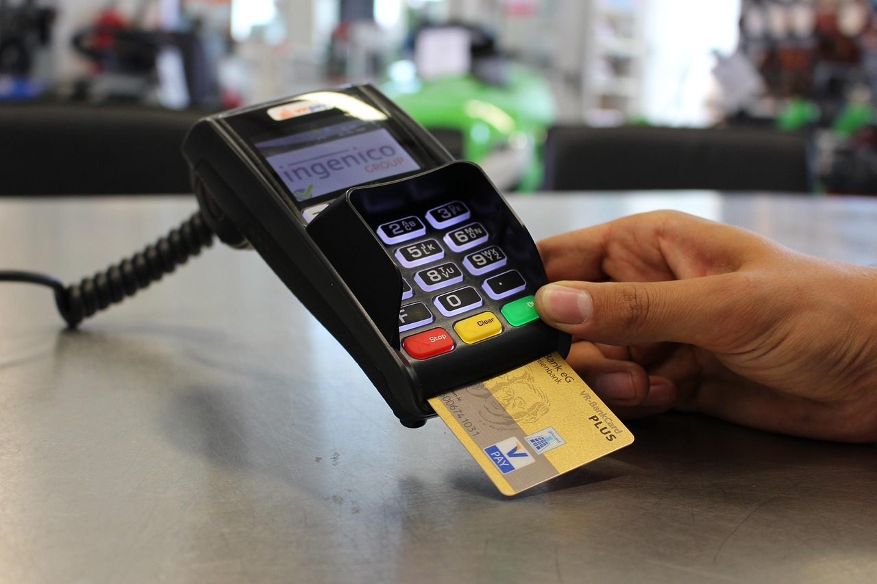 Hand hält Bankkarte, die in ein Kartenterminal mit beleuchtetem Tastenfeld gesteckt wird