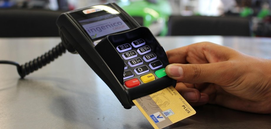 Hand hält Bankkarte, die in ein Kartenterminal mit beleuchtetem Tastenfeld gesteckt wird