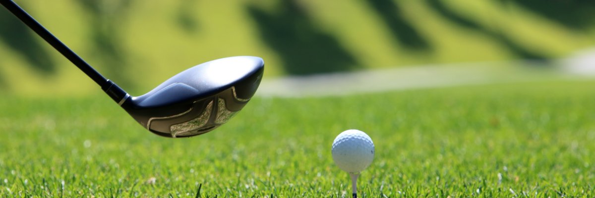 Golfball auf einem Abschlag mit Golfschläger im Hintergrund auf grünem Rasen