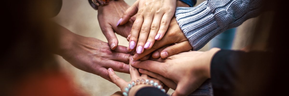 Mehrere Hände unterschiedlicher Personen liegen übereinander in einer Geste des Zusammenhalts