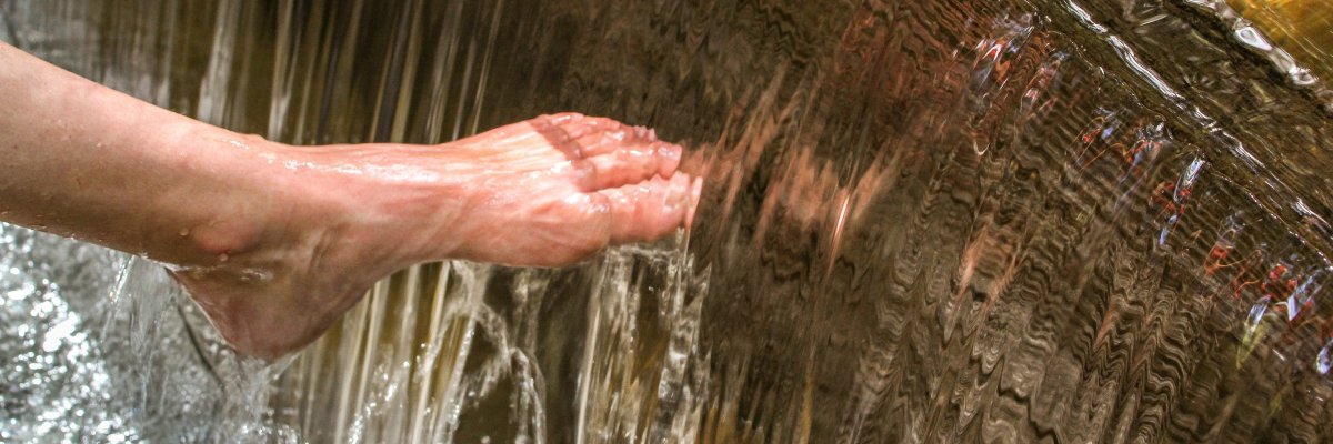 Fuß und Hand unter fließendem Wasser einer Kneippanlage