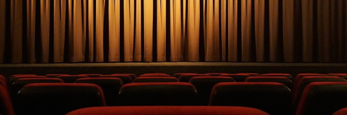 Geschlossener goldbrauner Kinobühnenvorhang vor Reihen roter Kinosessel
