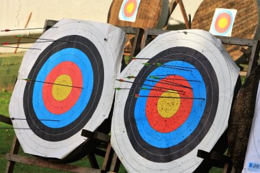Zwei runde Zielscheiben mit Pfeilen, die in verschiedenen Ringen stecken, auf Holzgestellen im Freien