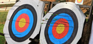 Zwei runde Zielscheiben mit Pfeilen, die in verschiedenen Ringen stecken, auf Holzgestellen im Freien