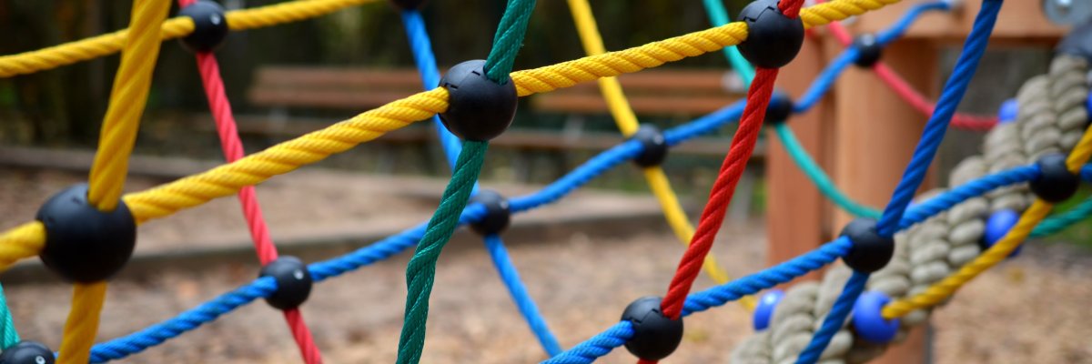 Nahaufnahme eines bunten Klettergerüsts aus Seilen mit schwarzen Verbindungsstücken auf einem Spielplatz