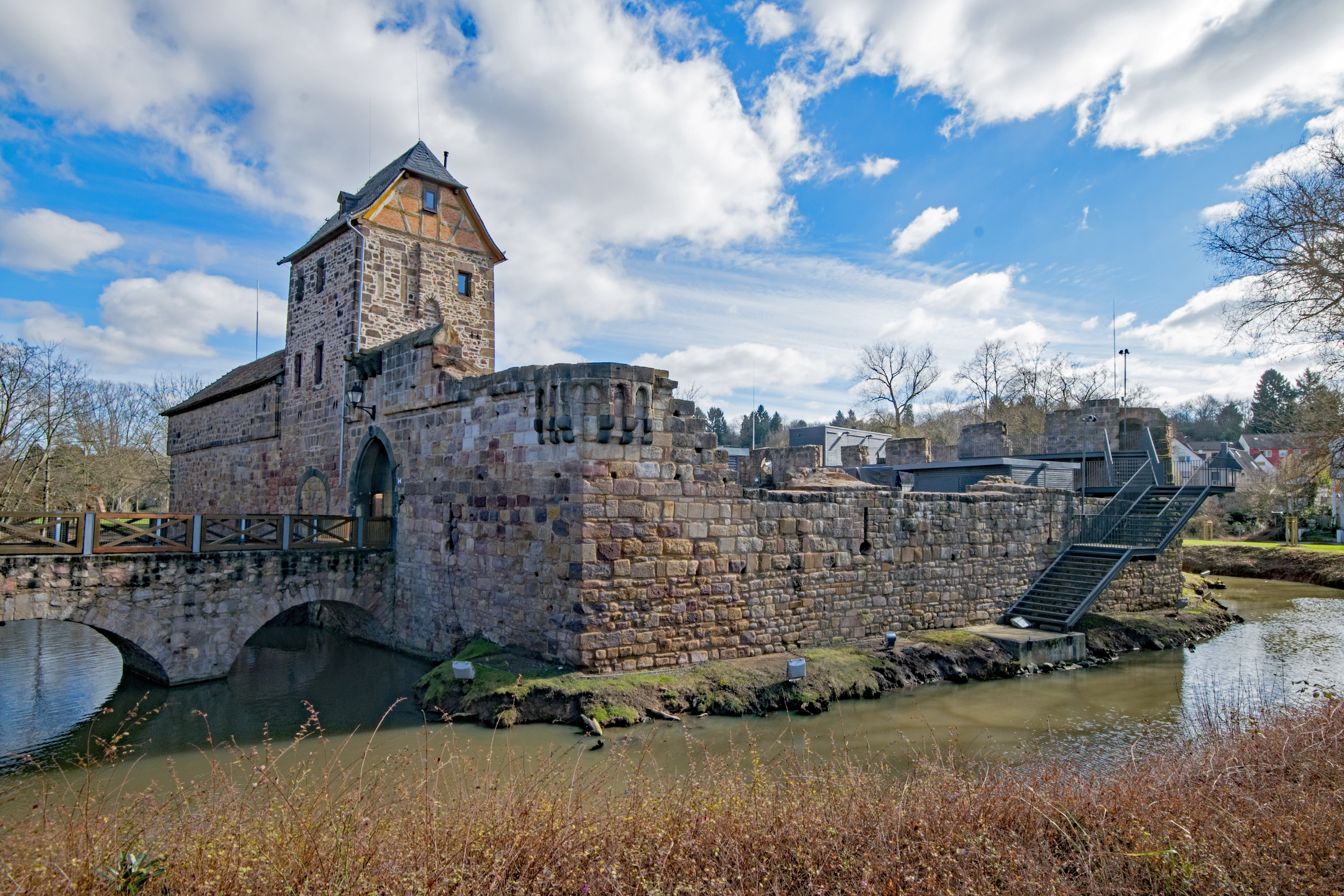 Wasserburg mit steinernen Mauern und Turm umgeben von Wasser und Brücke bei bewölktem Himmel