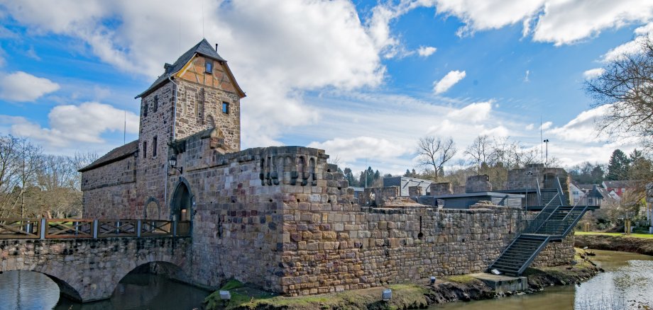 Wasserburg mit steinernen Mauern und Turm umgeben von Wasser und Brücke bei bewölktem Himmel