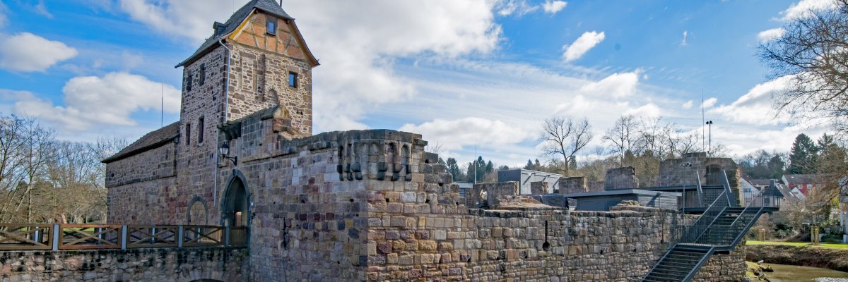 Wasserburg mit steinernen Mauern und Turm umgeben von Wasser und Brücke bei bewölktem Himmel