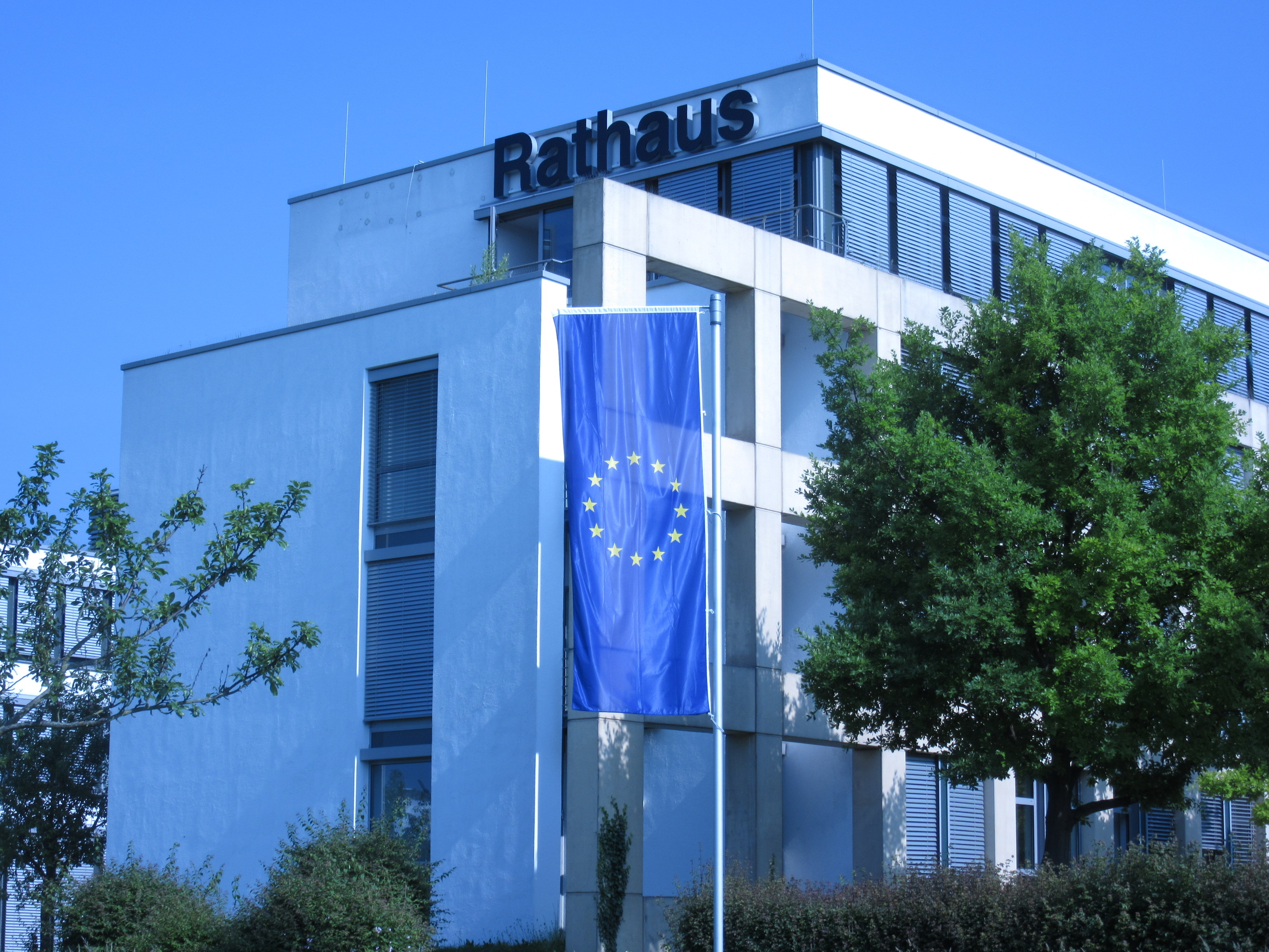 Rathaus Bad Vilbel mit Europafahne vor blauem Himmel und Bäumen