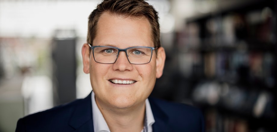 Porträt des Bad Vilbeler Bürgermeisters Sebastian Wysocki. Ein Mann mit dunklem Sakko und weißem Hemd vor unscharfem Hintergrund
