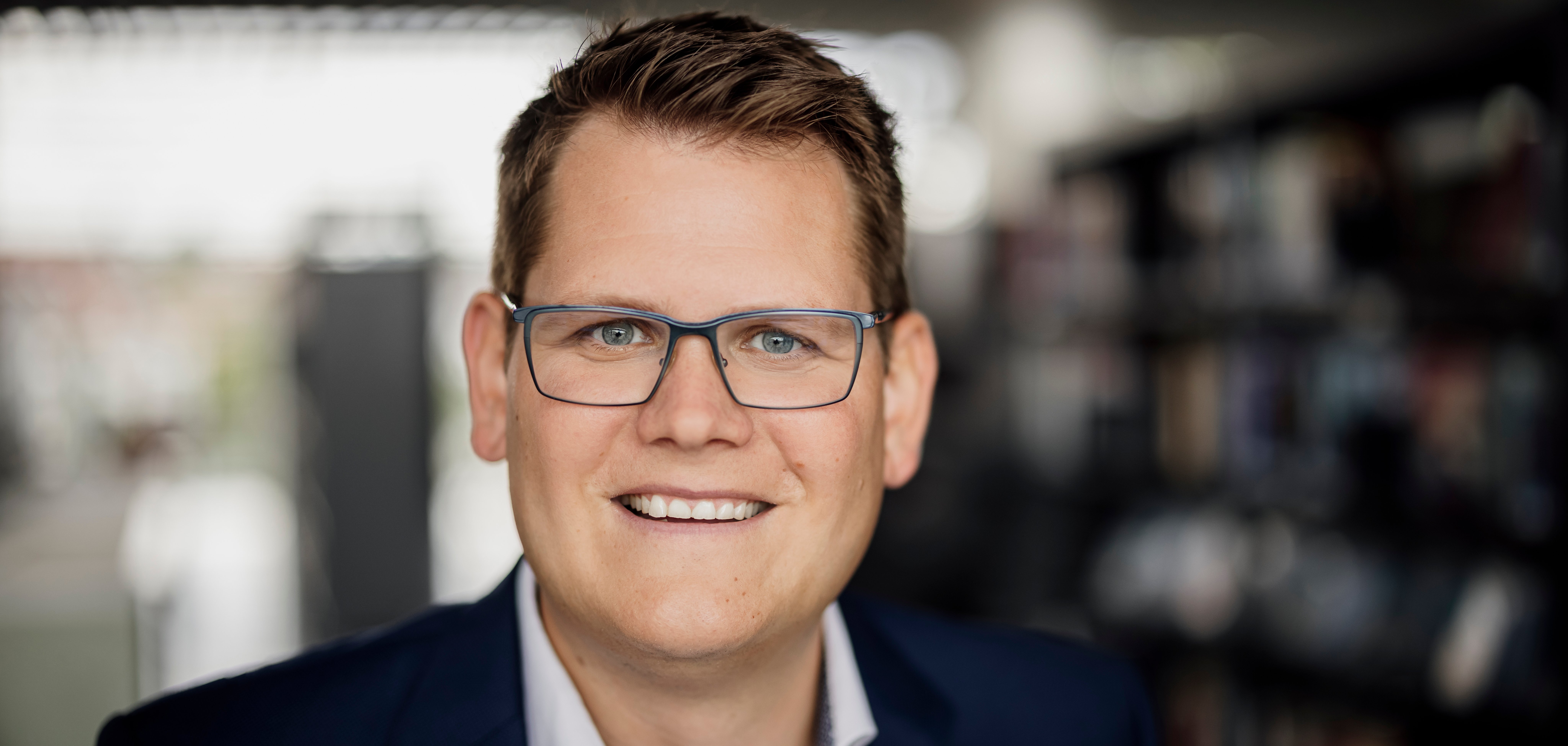 Porträt des Bad Vilbeler Bürgermeisters Sebastian Wysocki. Ein Mann mit dunklem Sakko und weißem Hemd vor unscharfem Hintergrund