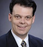 Porträt eines lächelnden Mannes (Ehrenbürgermeister Dr. Thomas Stöhr) mit dunklem Anzug, weißem Hemd und gemustertem Krawattenmuster vor neutralem Hintergrund