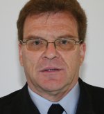 Porträt eines Mannes (Ehrenwehrführer Thomas Farr) mit Brille, kurz geschnittenem Haar und dunkelblauer Uniform vor hellem Hintergrund