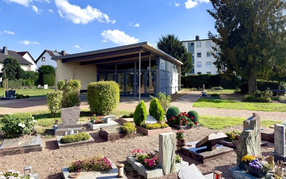 Moderner Friedhofsgebäudekomplex mit Glasfront und gepflegten Gräbern im Vordergrund unter blauem Himmel