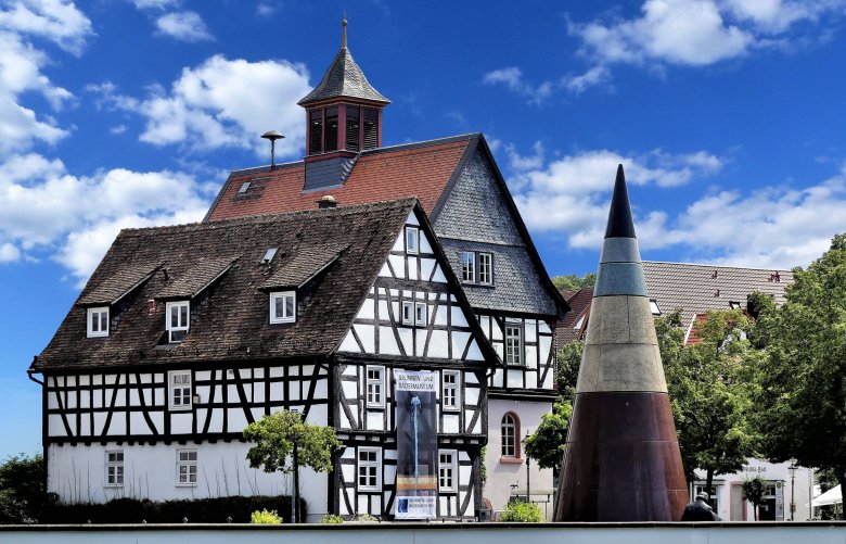 Historisches Rathaus Fachwerkhaus mit spitzem Turm und moderner kegelförmiger Skulptur davor unter blauem Himmel
